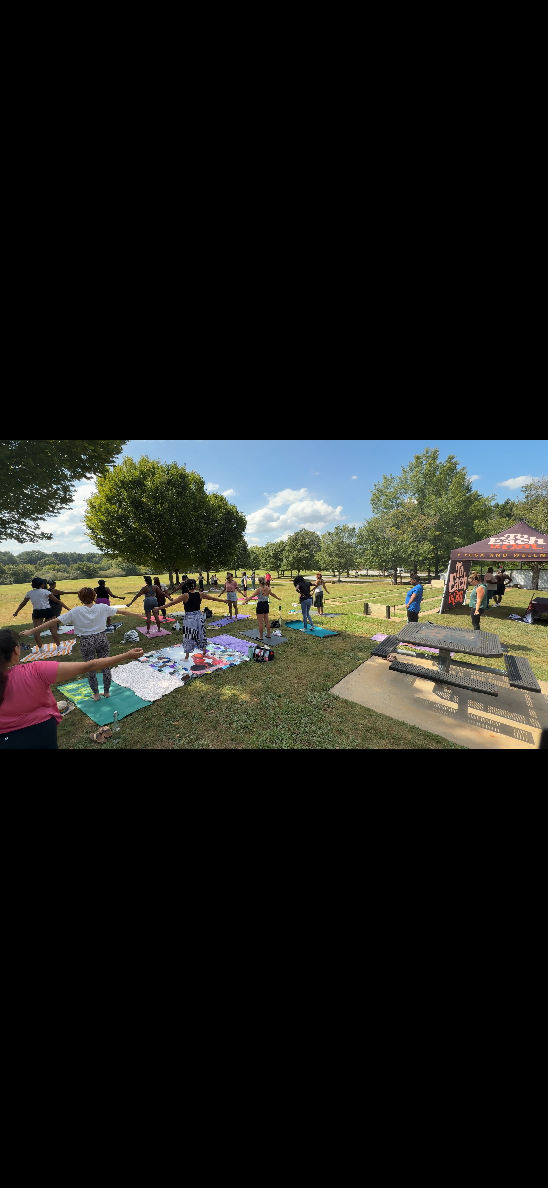 Participants stretching outdoors at Yoga in the Park beside the To Each Is Om tent